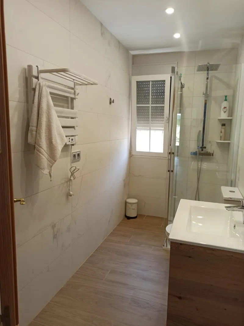 Baño con plato de ducha de carga mineral, mampara angular de doble apertura y suelo imitación madera, después de la reforma